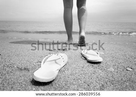 Black and white closeup photo of woman taking off flip flops and walking into the sea water