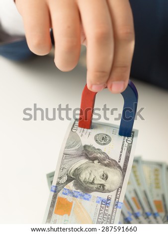 Closeup shot of male hand holding magnet and pulling money from stack