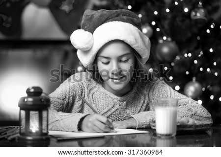 Black and white portrait of cute girl writing letter to Santa Claus at living room