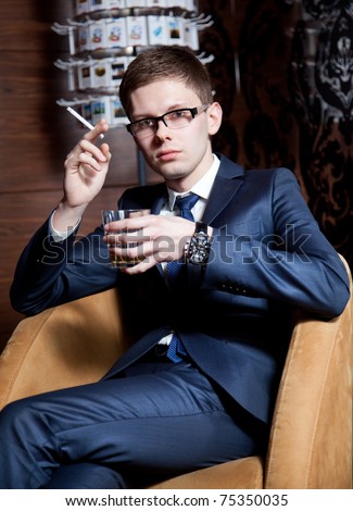 Young caucasian man in suit sitting with cigarette drinking cognac
