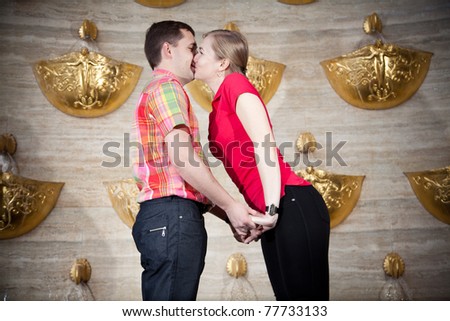 Two young people standing near golden fountain and kissing