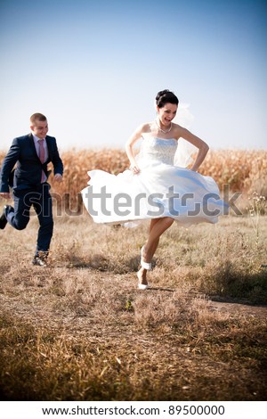 Young newly married couple chasing each other in field