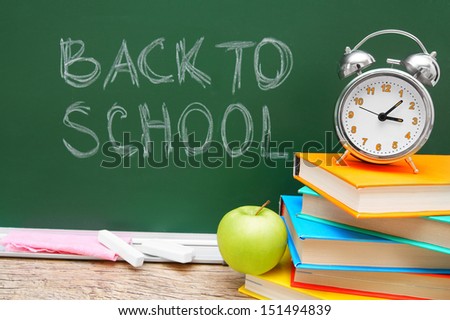 Apple, alarm clock and books against a school board. Back to school.