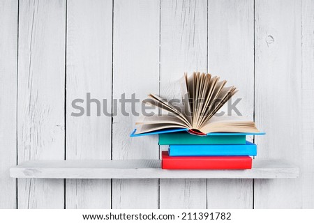 The open book on other multi-coloured books. On a wooden shelf. A wooden, white background.