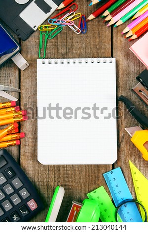 Back to school. A notebook and school tools around. Vertically. A wooden background.