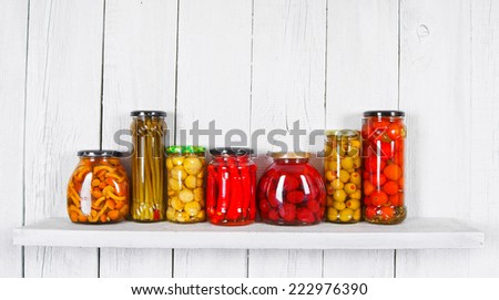Preserved food in glass jars, on a wooden shelf. Various autumn marinaded food