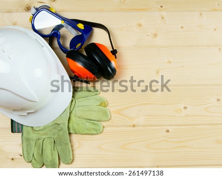 The working tools. A helmet, gloves and ear-phones on a wooden background.