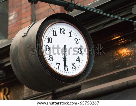 Wall clock, armed in iron tube, at the bricked wall of Victorian style house