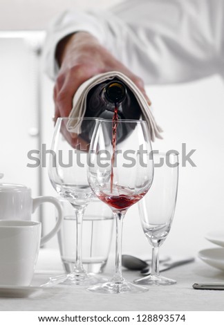 Pouring out red wine from a bottle in an elegant dining table setting at a restaurant or hotel