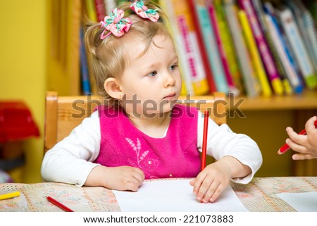 Child girl drawing with colorful pencils in preschool at the table  in kindergarten