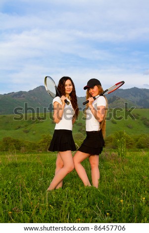 Two women tennis players in white T-shirt with rackets on the grass in sports