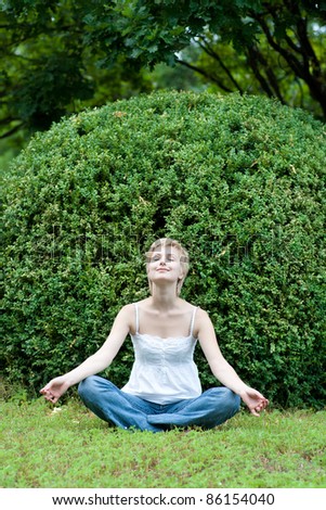 Image of meditating girl seated in pose of lotus on green grass