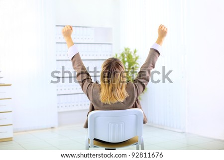 Business woman sitting in a chair and with her hands in the air celebrating success
