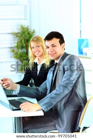 Young businessman smiles towards the camera while his colleagues meet in the background