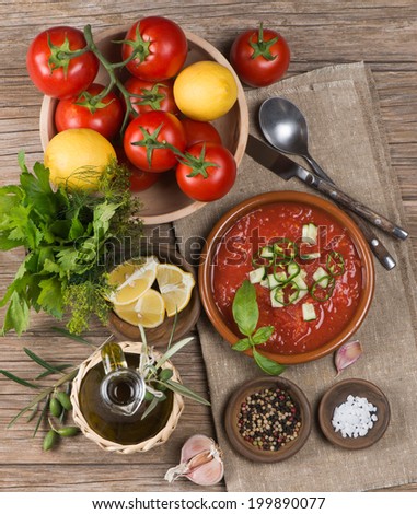 Bowl of gazpacho with  tomato and other vegetables on wooden table.  Top view.