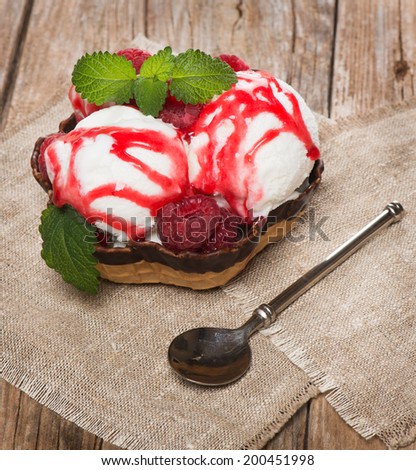 melted ice cream scoops with jam and fresh  raspberries on a wooden table