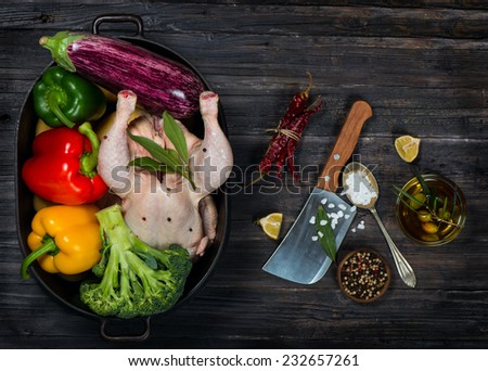 Uncooked chicken with vegetables in a black casserole on a old black wooden table  top view