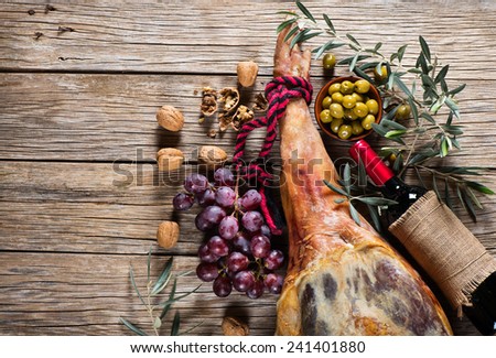 whole leg of smoked ham, bottle of red wine, grapes, walnuts and pickled olives on a old wooden background with space for text, top view
