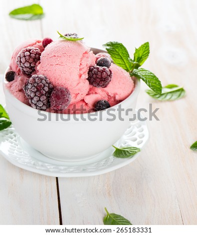 Ice cream dessert served with frozen berries and mint in a white bowl. Selective focus.