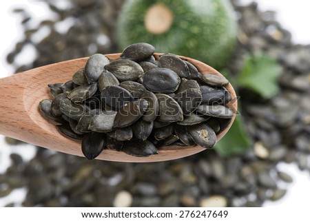 Pumpkin seeds in a wooden spoon on a background of spilling seeds and pumpkin