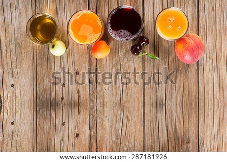 Four varieties of juice in glasses and fresh fruits on a rustic wooden background,   with space for text, top view.