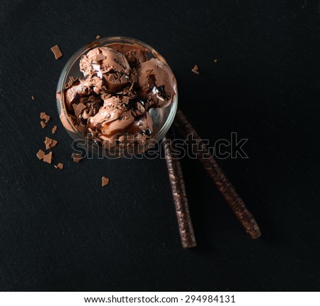Top view of chocolate ice cream with wafer sticks, sauce and chips on a black slate board