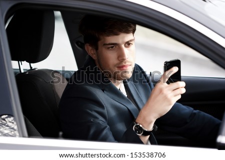 Young businessman in blue suit sitting in a new car and holding the mobile phone