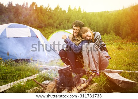 Portrait of happy couple sitting near by the campfire with the tents on background, Montenegro