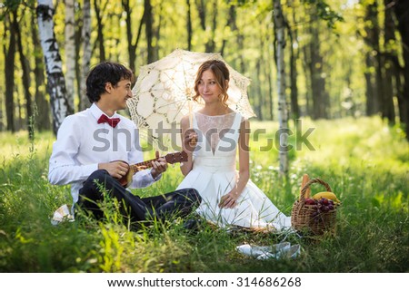 Happy lovely couple on their wedding day in the summer forest. Groom playing on ukulele