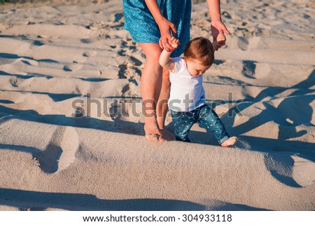 Baby girl learn to walk with her mother on the beach. mother holding child hands