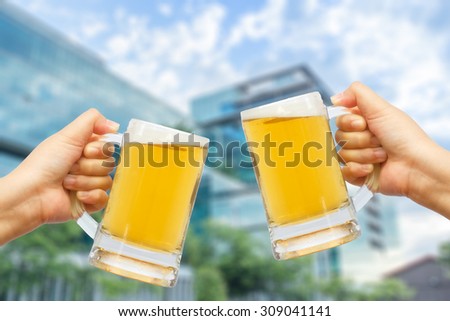 Cheers beer for celebration in your success with burred building background.