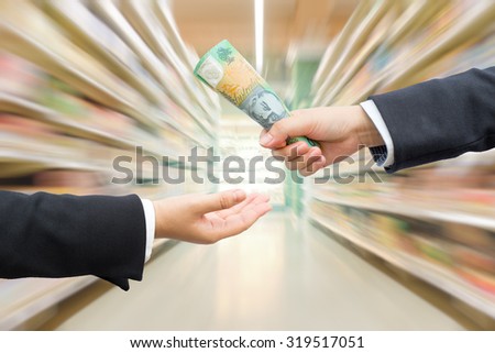 Hands of businessman passing Australian dollar (AUD) banknote with blurred warehouse or supermarket background.