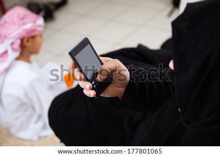 Happy Arabic mother using smart phone and her son together at home.