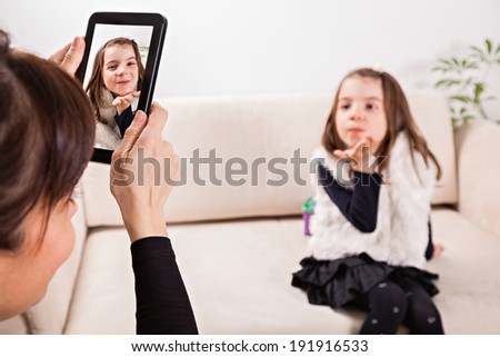 Mother taking photo of her daughter with tablet. Focus is on tablet.