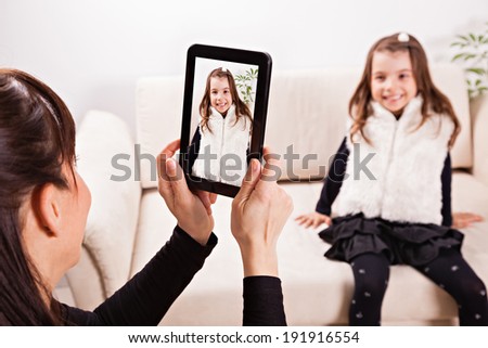 Mother taking photo of her daughter with tablet. Focus is on the tablet.