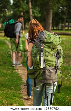 Three Young Tourists With Backpacks Walking Through The Woods