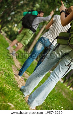 Three Young Tourists With Backpacks Walking Through The Woods