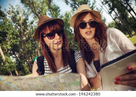 Two Tourist Girls In Nature Browsing Map Using Digital Tablet