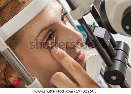 Ophthalmologist In Exam Room With Young Woman Looking Into Eye Test Machine