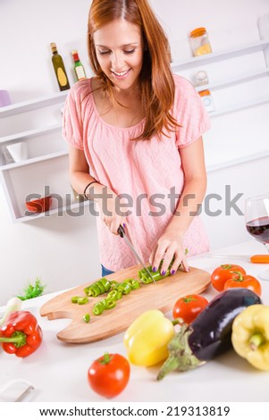 Beautiful Young Housewife In The Kitchen Slicing Vegetables On Chopping Board