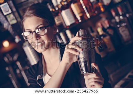 Female Bartender Making Cocktail Using Shaker In Pub.