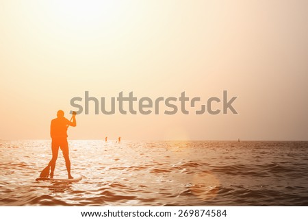 Silhouette Of Man Paddleboarding At Sunset