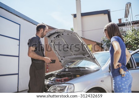 Auto Mechanic With Female Customer Checking Out Engine Problems Using Digital Tablet