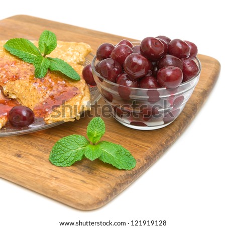 frozen cherries in a glass bowl and pancakes with cherry jam with a sprig of mint on a cutting board