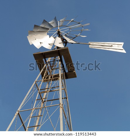 Angled and close up shot from the ground of an old fashioned power windmill against a clear blue sky.