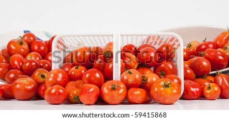 A studio front panoramic close-up view of a basket of ripe red field tomatoes on its side flanked by two angled dishes of tomatoes.