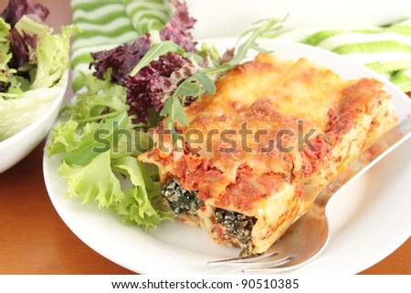 Freshly baked spinach and ricotta cannelloni with a simple green salad. On a green striped cloth and a wooden table.