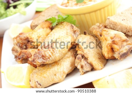 Chicken wings served with coleslaw and a side salad. On a square plate and garnished with lemon and parsley.