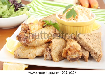 Chicken wings served with coleslaw and a side salad. On a square plate and garnished with lemon and parsley.