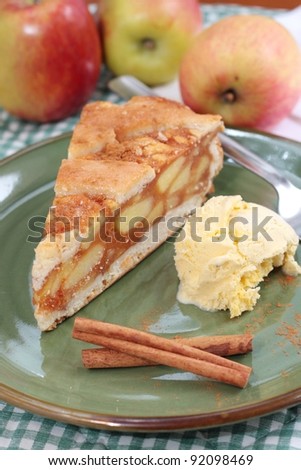 A slice of apple pie with a lattice pastry crust. Decorated with cinnamon sticks and fresh apples.